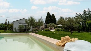 A swimming pool with a stone edge, a white building, and a grassy area with trees and shrubs. - Holiday Home "Le Cabanon de Modène" with Mountain View, Wi-Fi and Air Conditioning (Modène)