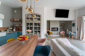 A modern living space with a wooden dining table, colorful chairs, a sofa, a TV mounted on the wall, and a kitchen area with cabinets and a fruit bowl. - Holiday Home 'Le Cabanon De Modène' with Mountain View, Wi-Fi and Air Conditioning (Modène)