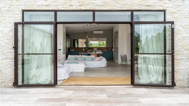 A modern interior with a stone wall, a sofa set, and a kitchen area visible through large glass doors. - Holiday Home "Le Cabanon de Modène" with Mountain View, Wi-Fi and Air Conditioning (Modène)