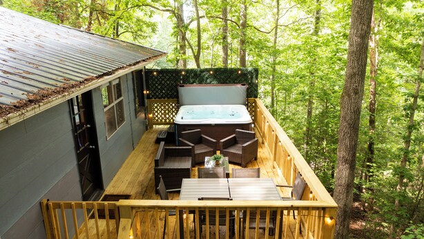 Eine Holzterrasse mit Whirlpool, Sitzgelegenheit und Blick auf den Wald.