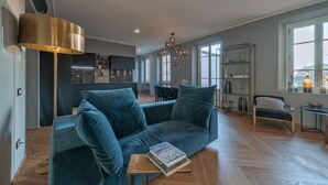 A modern living room with a blue sofa, a coffee table with books, a floor lamp, and a dining area in the background. - Apartments Florence - Repubblica Exclusive with Balcony (Florence)