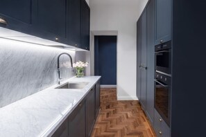 A narrow kitchen with dark cabinets, a marble countertop, and a herringbone wood floor. - Apartments Florence - Blue Lily with terrace (Firenze)
