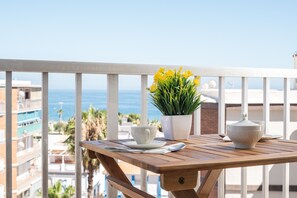 Ein Balkon mit Tisch, Topfpflanze, Tasse und Schüssel.