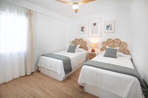 Une chambre avec deux lits, un ventilateur de plafond, une fenêtre avec des rideaux et des œuvres d’art mural.
