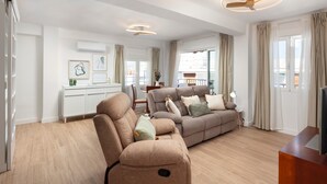 Una sala de estar moderna con un sofá, un sillón reclinable, un mueble para televisión y un comedor con mesa y sillas.