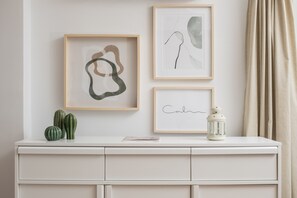 Une commode blanche ornée de trois œuvres d’art encadrées, d’un cactus et d’une lanterne.
