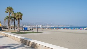 Una playa con palmeras, cielo despejado y un paisaje urbano a lo lejos.