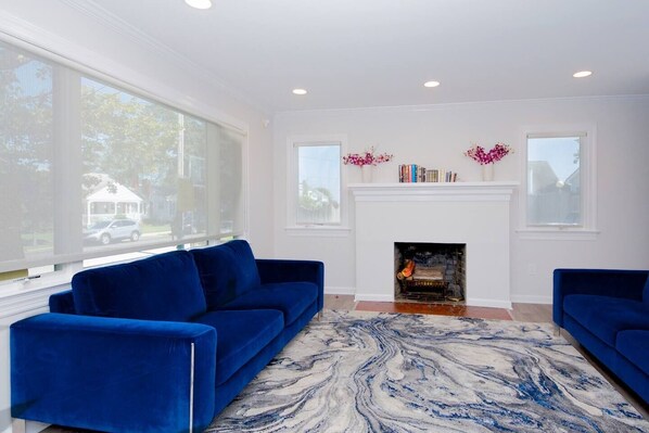 A living room with a fireplace, two blue sofas, a marble-patterned rug, and large windows.