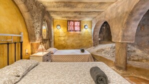 A room with a bed, a nightstand, a lamp, a window with curtains, and a stone archway. - Holiday Home 'Ermita De Las Eras' with Mountain Views, Wi-Fi and Air Conditioning (Algarinejo)