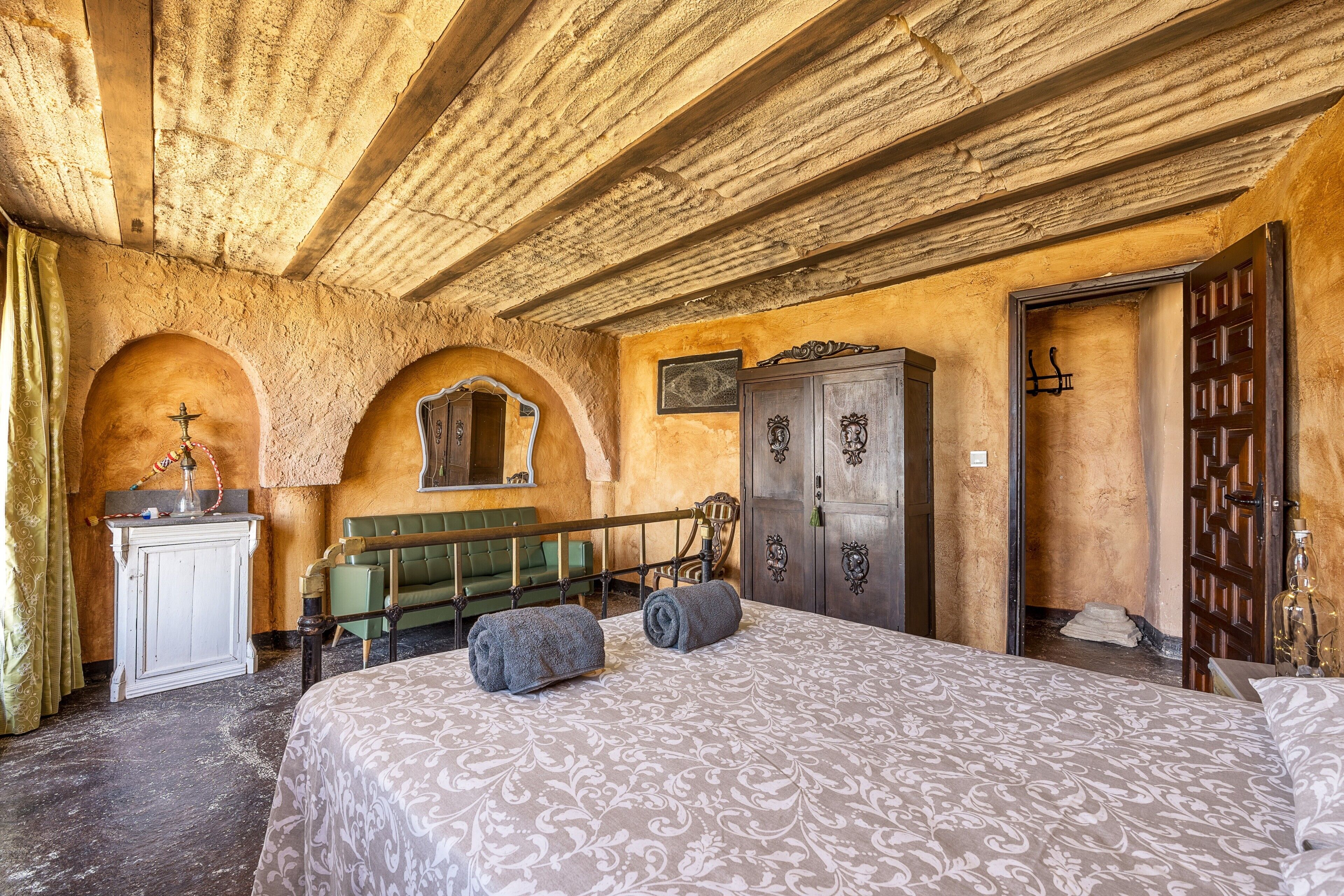 Una habitación con una cama, un banco de madera, un armario y una puerta.