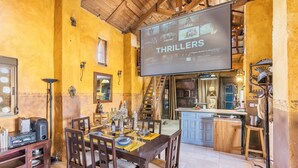 A dining area with a wooden table set for four, a projector screen displaying 'THRILLERS,' and a kitchen in the background. - Holiday Home 'Ermita De Las Eras' with Mountain Views, Wi-Fi and Air Conditioning (Algarinejo)