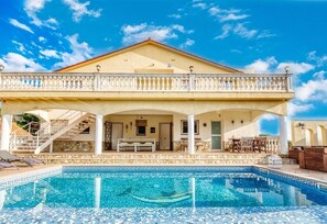 A two-story building with a swimming pool, outdoor seating, and a covered patio area.
