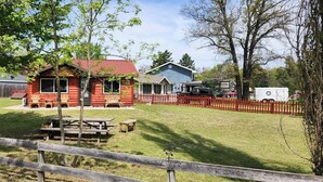En rød hytte med et picnicbord og stole, en blå bygning, og et rødt stakitterhegn.