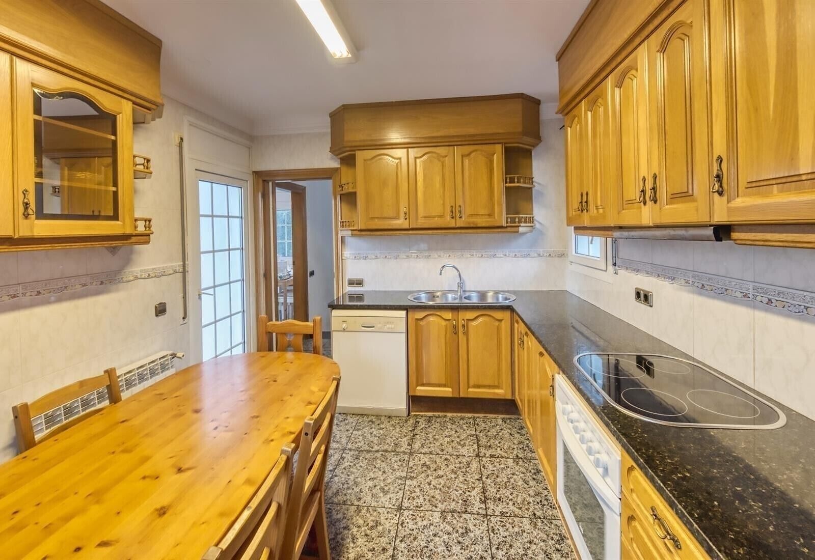 Une cuisine avec des meubles de rangement en bois, un plan de travail noir, un évier et une table à manger avec des chaises.