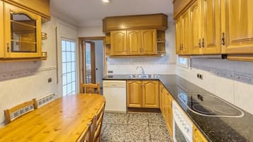 Een keuken met houten kasten, een zwart aanrecht, een spoelbak en een eettafel met stoelen.