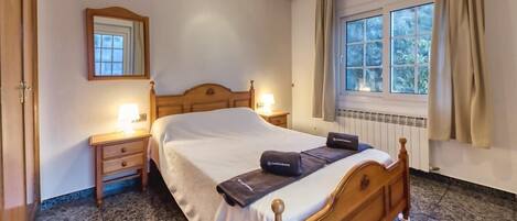 Une chambre à coucher avec un lit en bois, des tables de chevet, un miroir, une fenêtre avec des rideaux et un radiateur.