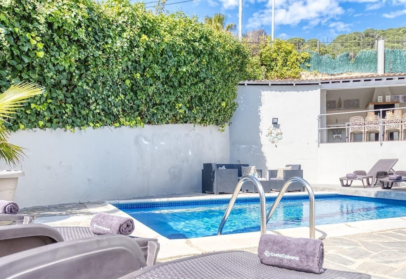 A swimming pool with lounge chairs and a white wall with greenery.