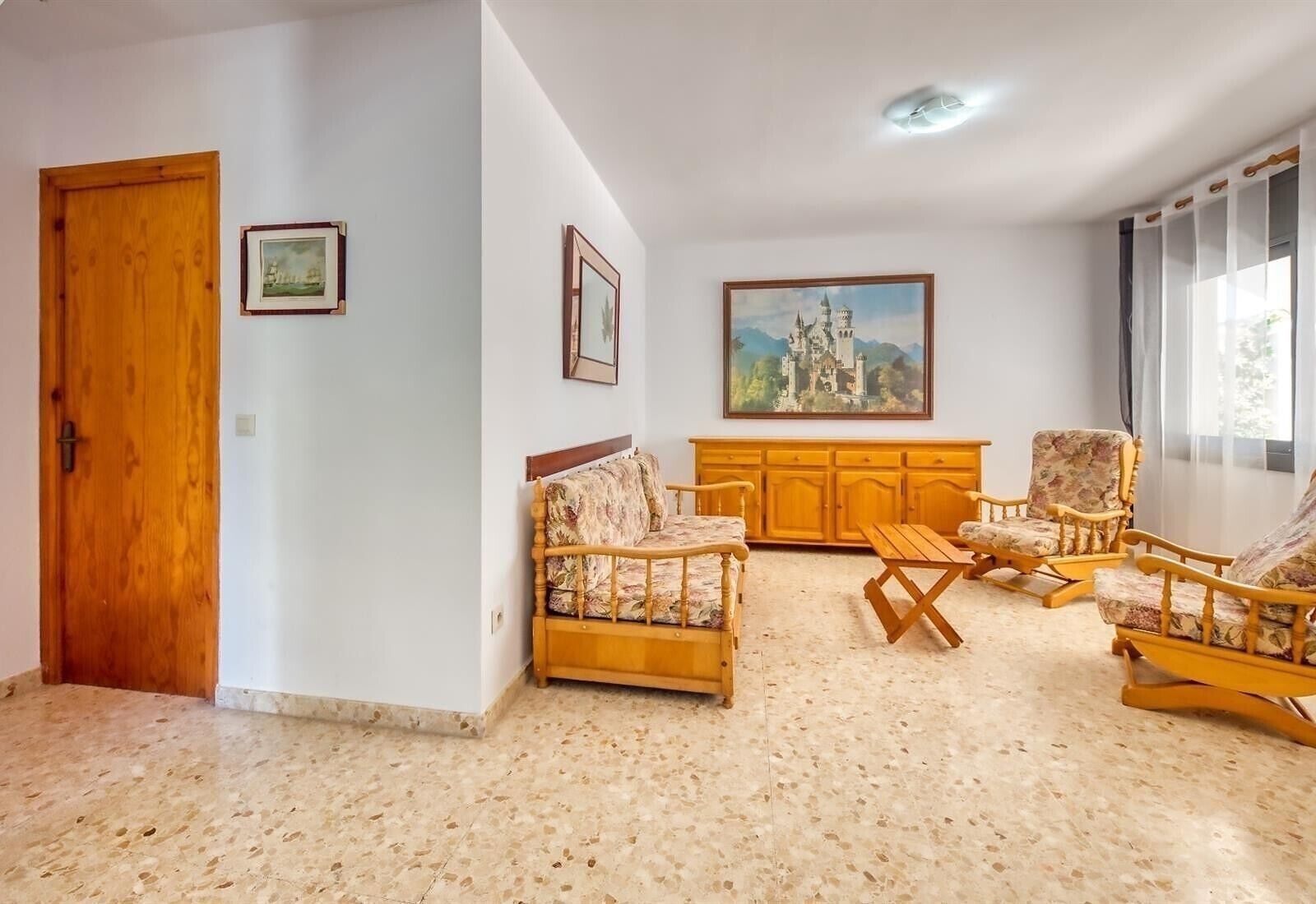 Un salon avec une porte en bois, deux fauteuils, un canapé, un meuble en bois et un tableau accroché au mur.