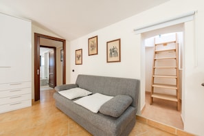 Una sala de estar con un sofá gris, dos almohadas, una escalera de madera y tres cuadros en la pared.