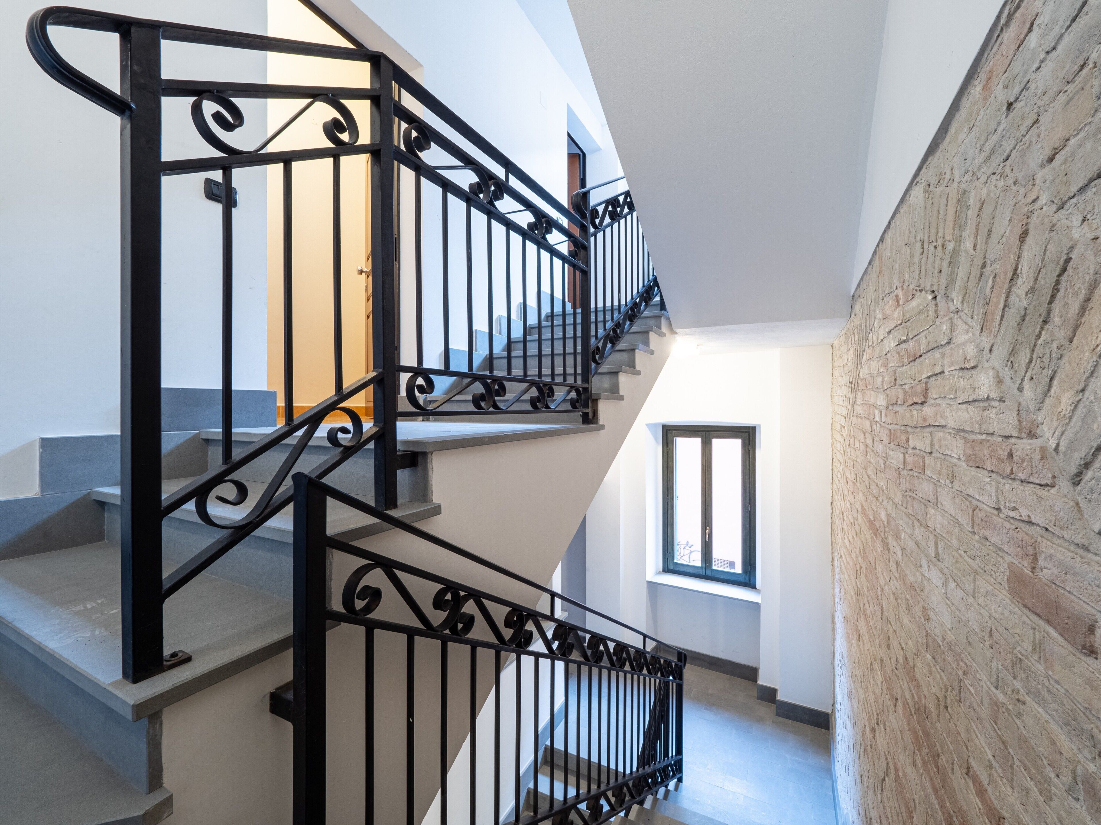 A staircase with black railings, a brick wall, and a window.