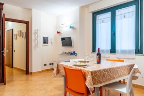 Un comedor con una mesa lista para dos, un televisor montado en la pared y una ventana con cortinas.
