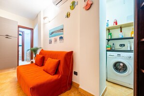 Un dormitorio con cama, lavadora, planta en maceta y vista al exterior.