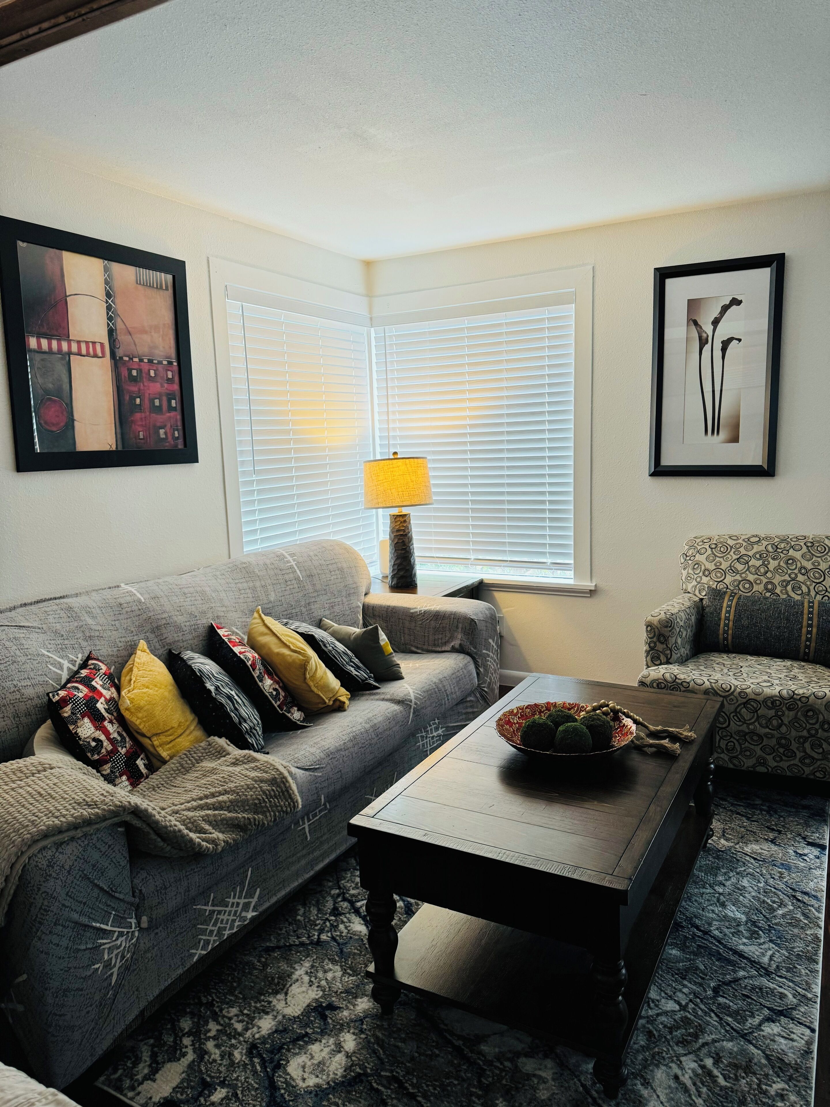 A living room with a grey sofa, patterned armchairs, a wooden coffee table, and a lamp.