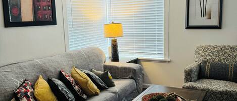 A living room with a grey sofa, patterned armchairs, a wooden coffee table, and a lamp.