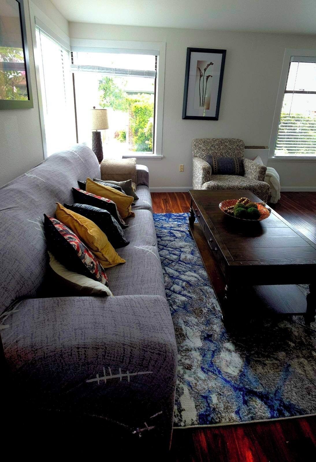 A living room with a grey sofa, patterned cushions, a blue and white rug, a wooden coffee table, and a patterned armchair.