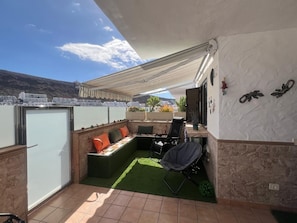A balcony with a seating area, a table, and a grill.
