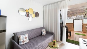 A modern living room with a grey sofa, a coffee table, and a view of a hillside. - Vacation Apartment 'Aloe Puerto Rico Beach' with Sea View, Wi-Fi and Air Conditioning (Puertorico -Mogan)