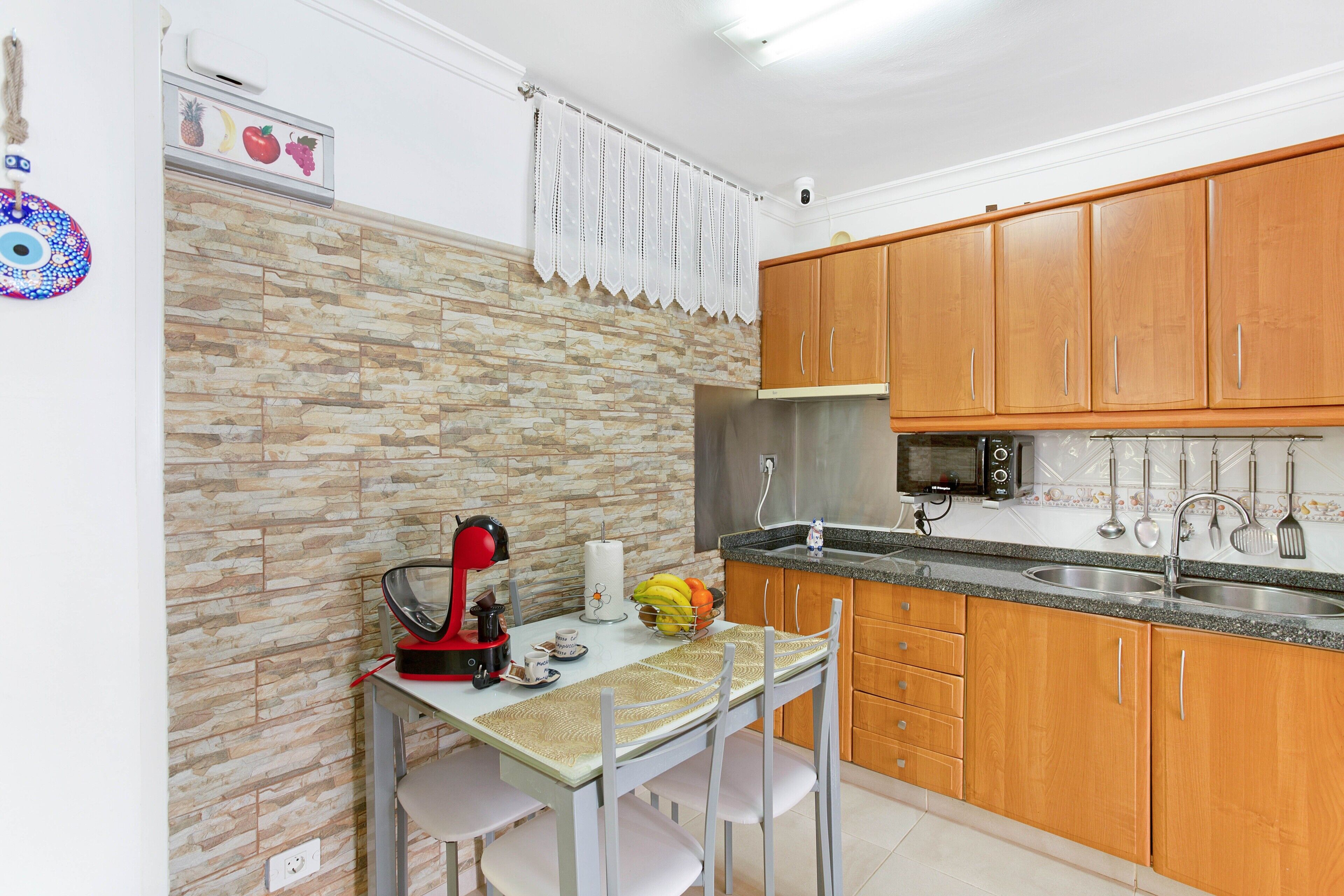 A kitchen with a stone backsplash, wooden cabinets, a stainless steel sink, and a red coffee maker.