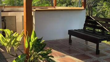 A wooden bench in a sunlit patio area with tiled flooring and potted plants.