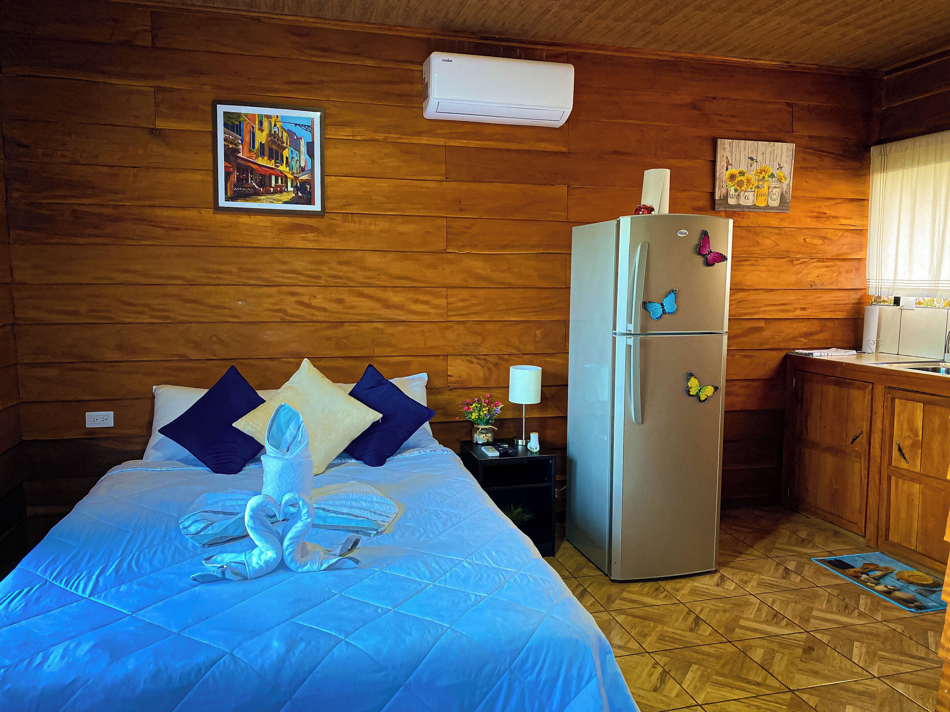 A room with a bed, a refrigerator, wooden walls, and a window.