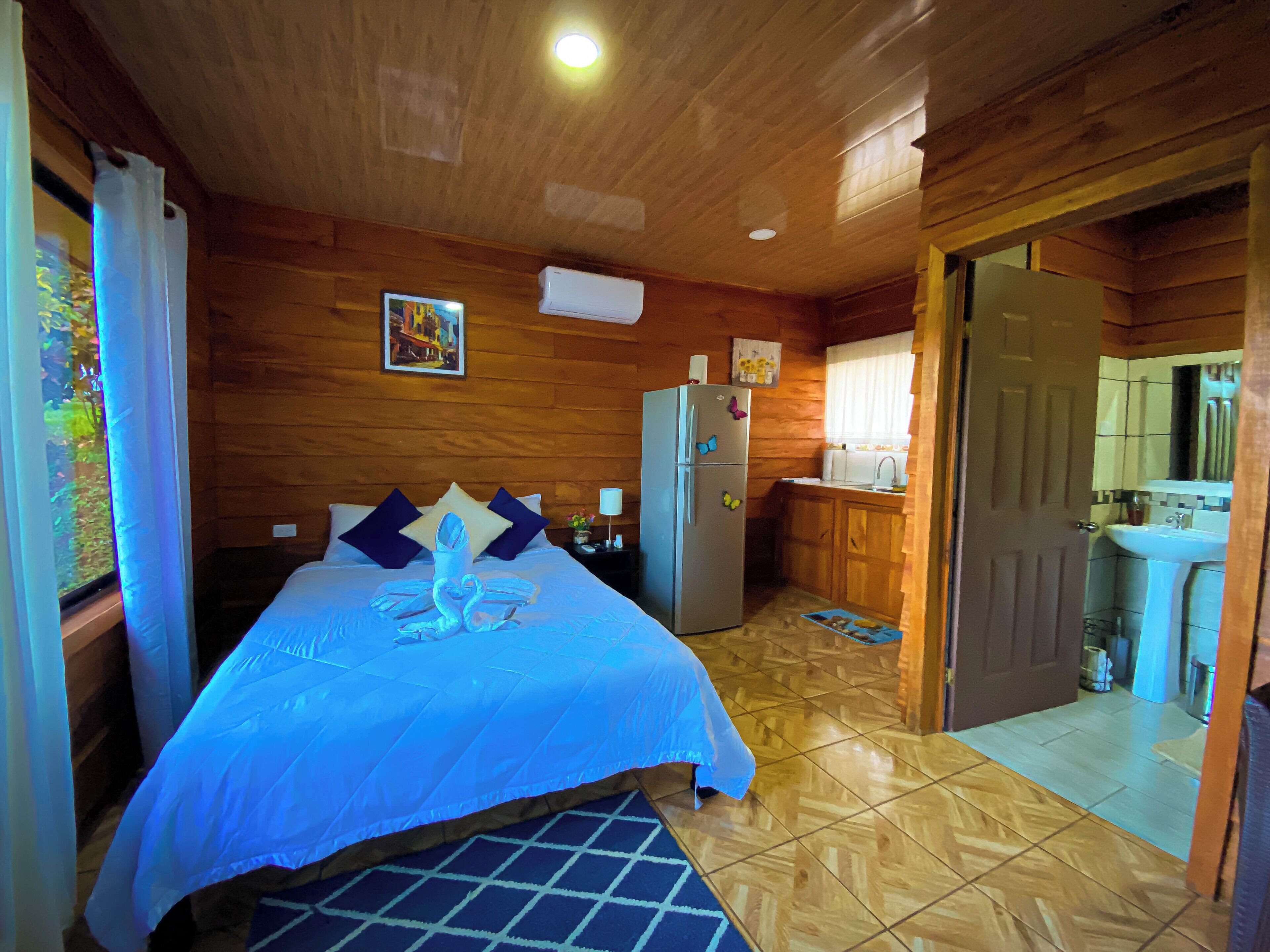 A wooden cabin with a bed, a refrigerator, a sink, and a door leading to another room.