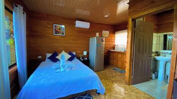 A wooden cabin with a bed, a refrigerator, a sink, and a door leading to another room.