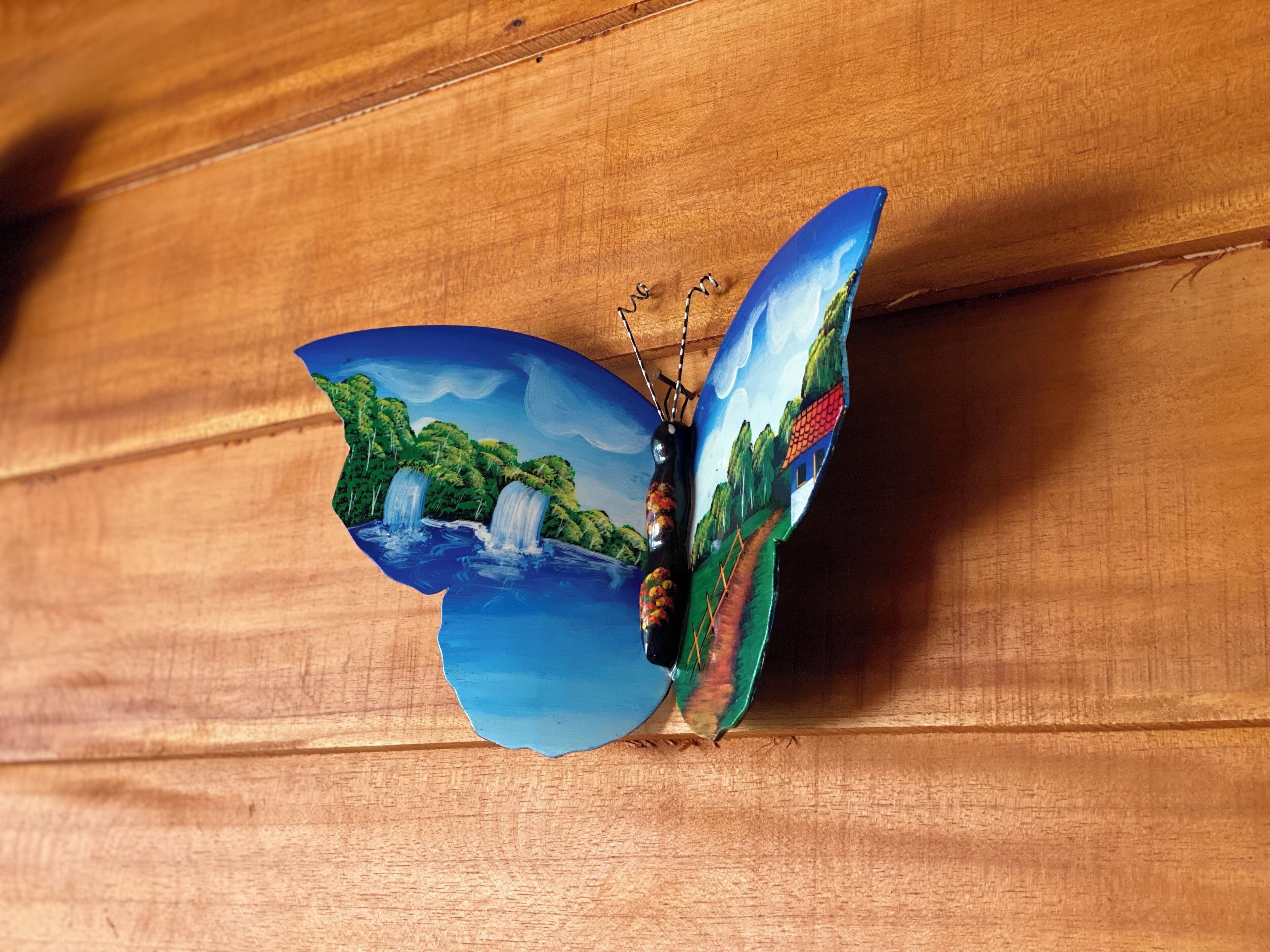 Un papillon aux ailes ornées d’un motif représentant un paysage, posé sur une surface en bois.