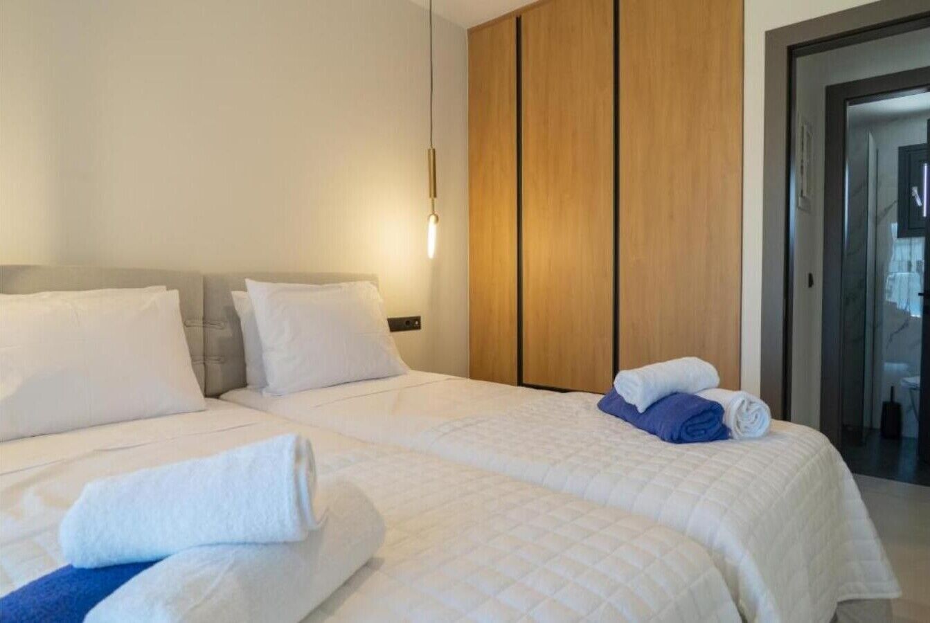 Een hotelkamer met twee bedden, een houten garderobe en een glazen deur naar een badkamer.