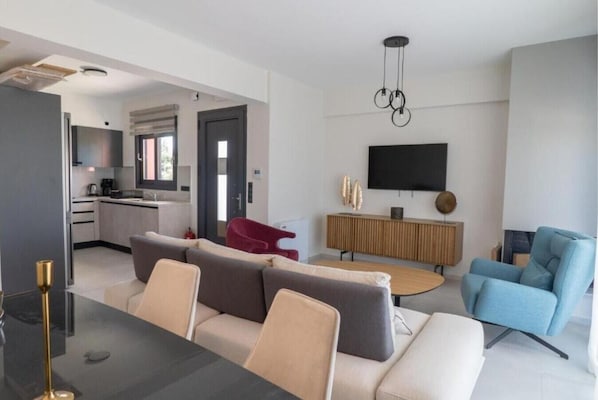 Una sala moderna con un sofá, una butaca roja, un televisor y un comedor con una mesa.