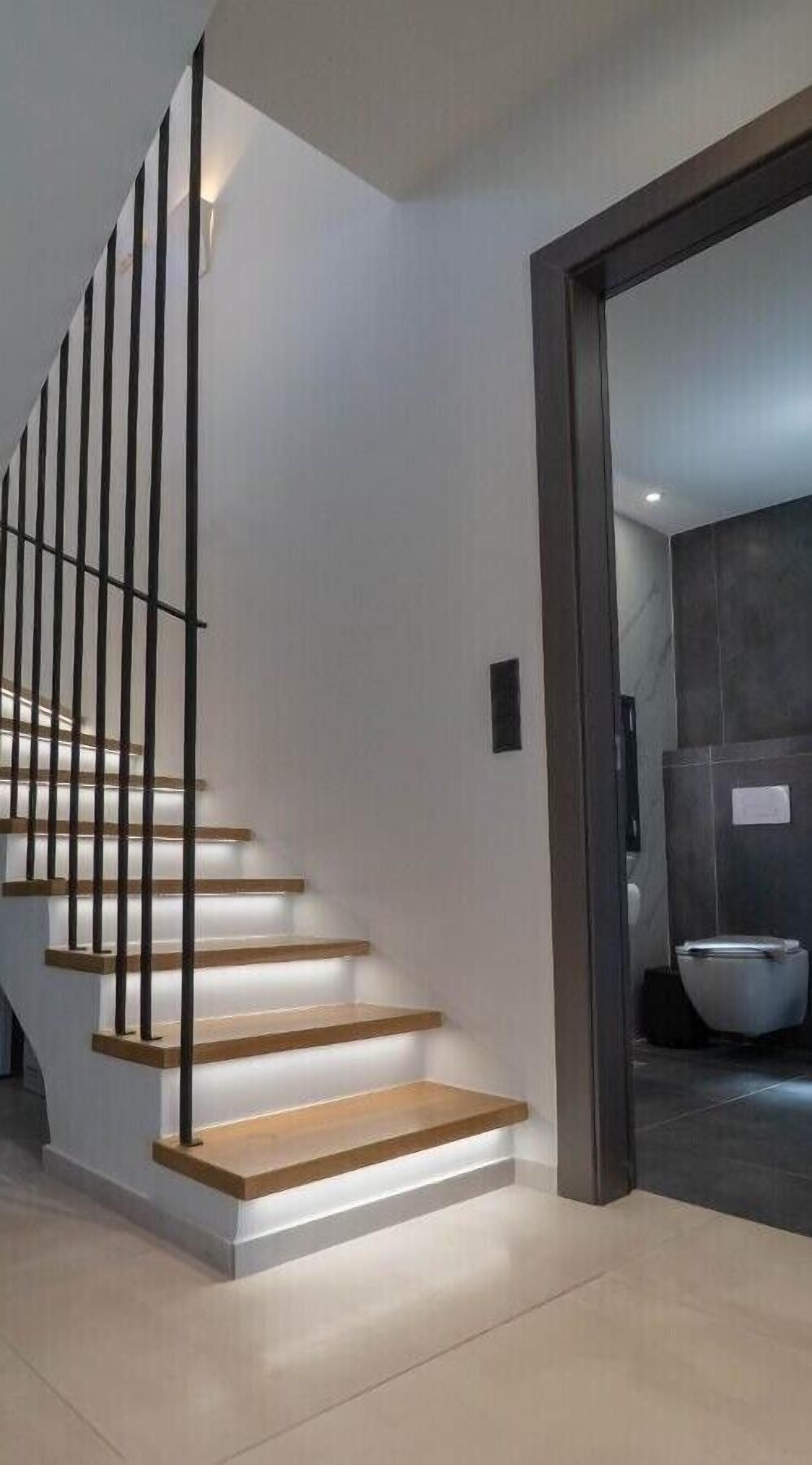 A modern staircase with wooden steps and black railings, leading to a room with a dark-toned wall and a large bowl.