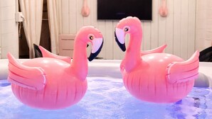 Kaksi vaaleanpunaista, ilmatäytteistä flamingo-lelua porealtaassa, jonka takana on valkoisilla laatoilla verhoiltu seinä ja jonka yläpuolella on seinälle asennettu litteänäyttöinen televisio.