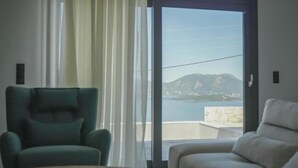 Una habitación con vistas al mar y a las montañas, un sillón verde y un sillón blanco.