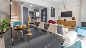 Una sala moderna con una mesa de vidrio, sofás, un televisor y una cocina al fondo.