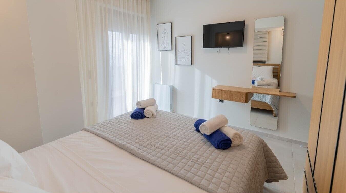 Une chambre d’hôtel avec un lit, un téléviseur fixé au mur, un miroir et une étagère avec des serviettes.