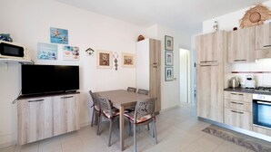 A modern kitchen with wooden cabinets, a dining table with chairs, a flat-screen TV, and a microwave. - Holiday Home 'Villetta Serena' with Shared Terrace, Wi-Fi and Air Conditioning (San Teodoro)