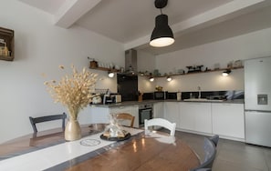 A modern kitchen with white cabinets, a dining table with chairs, and a hanging light fixture.