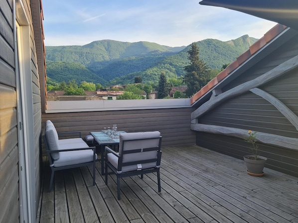 A wooden deck with a table and chairs, overlooking a mountainous landscape.