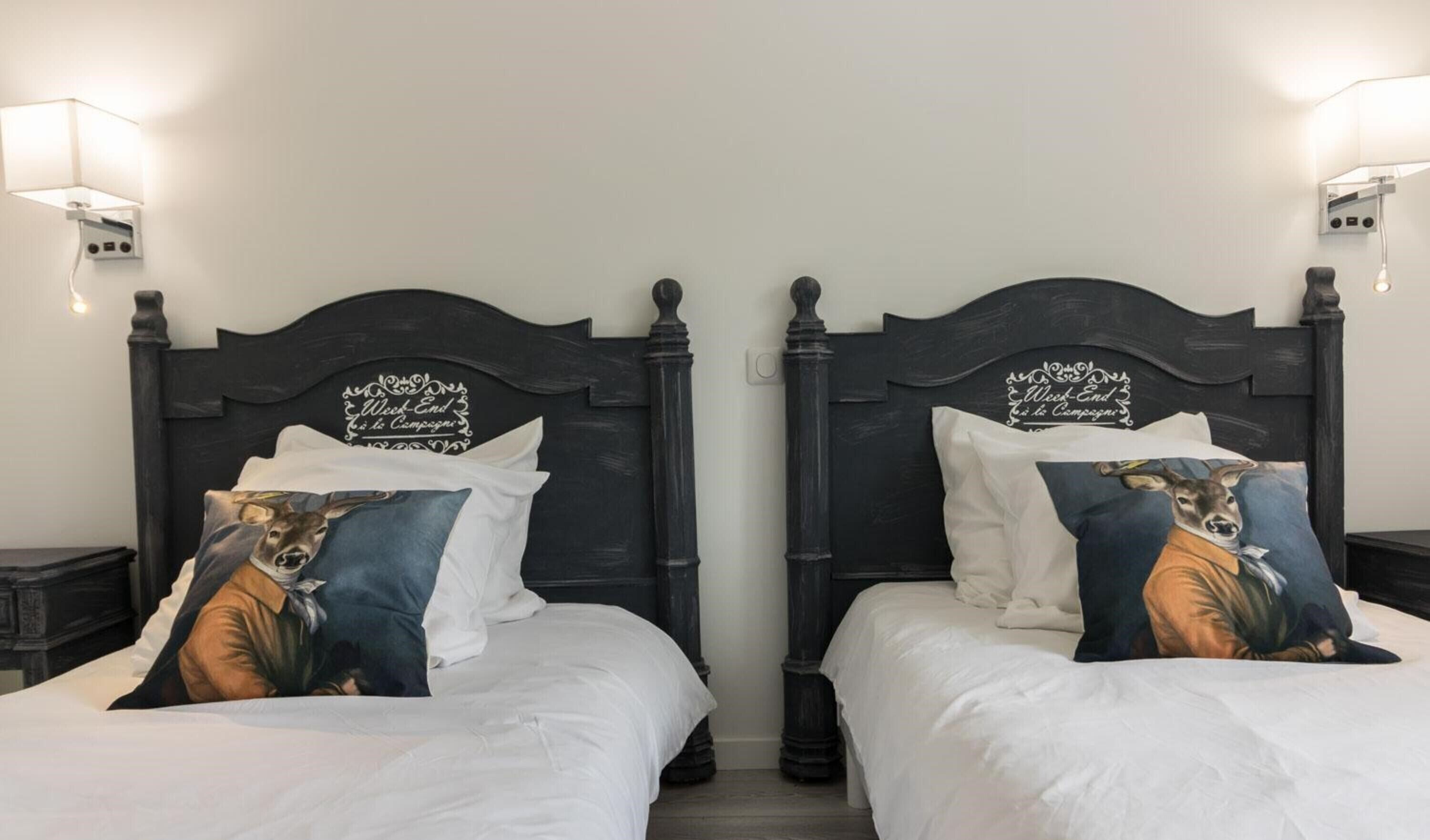 Un lit double doté d’une tête de lit ornée d’un motif décoratif et d’un texte, d’un couvre-lit blanc et d’un oreiller à motifs animaliers.