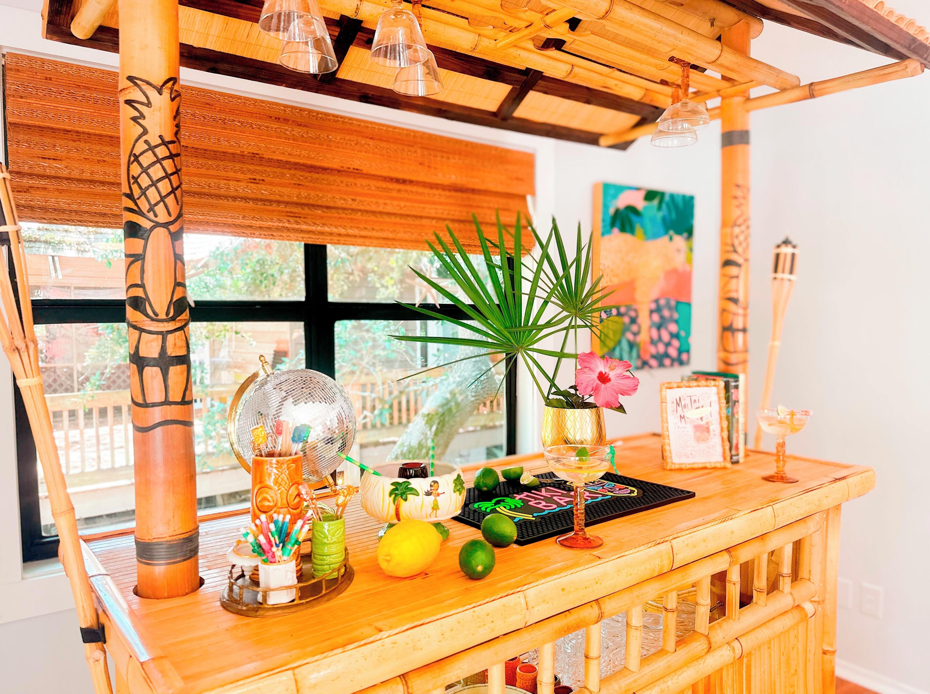 A wooden bar area with a tropical theme, including a tiki bar, a potted plant, and a cocktail glass.