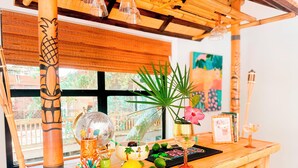 Una zona de bar de madera con temática tropical, que incluye un bar tiki, una planta en maceta y una copa de cóctel.